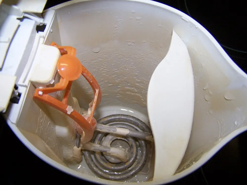 Blik in een geopende waterkoker met een gekalkt verwarmingselement, een beige kalklaag op de bodem en kalkvlekken op de binnenwand
