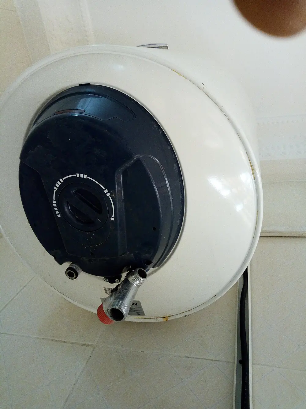 Witte elektrische wandboiler van onderen gezien, met een donkere kap, een draaiknop met temperatuurschaal en twee wateraansluitingen