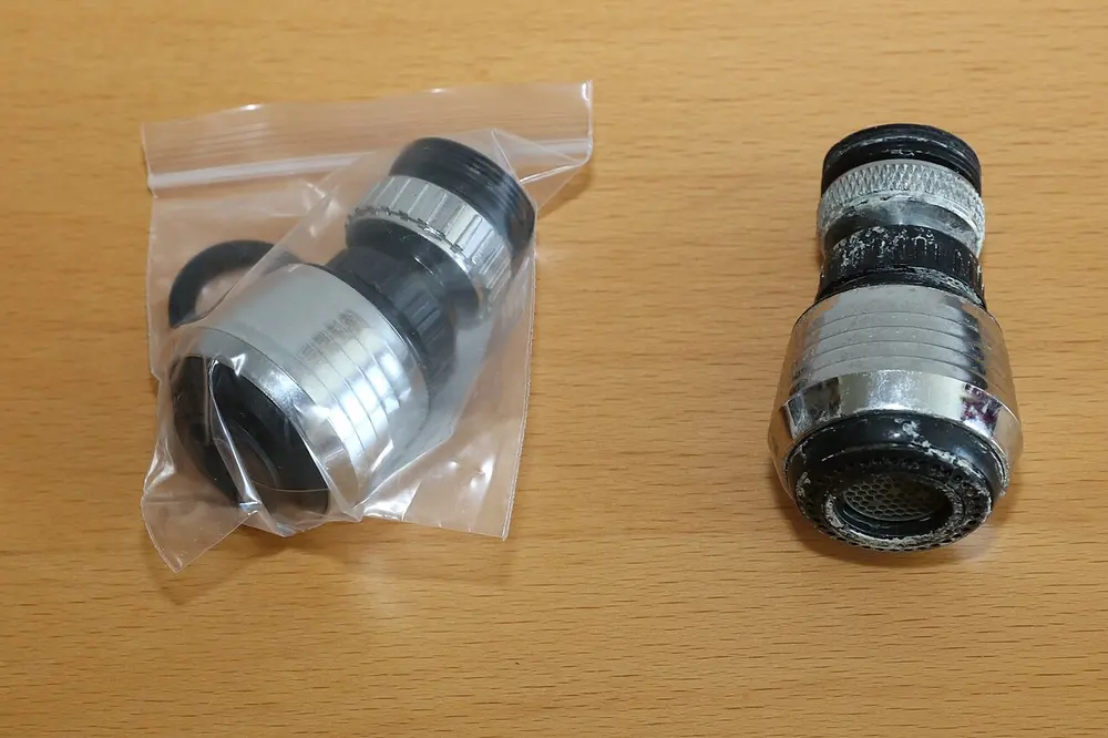 Twee kraanmondstukken op een houten tafel: links een nieuw exemplaar in een plastic zakje, rechts een oud mondstuk met kalkresten